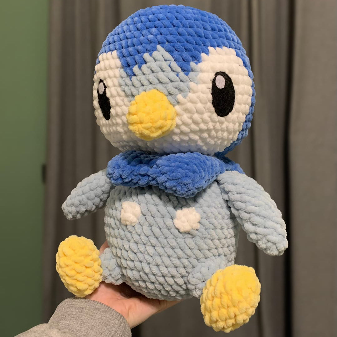 Crocheted penguin plush toy held in front of a curtain